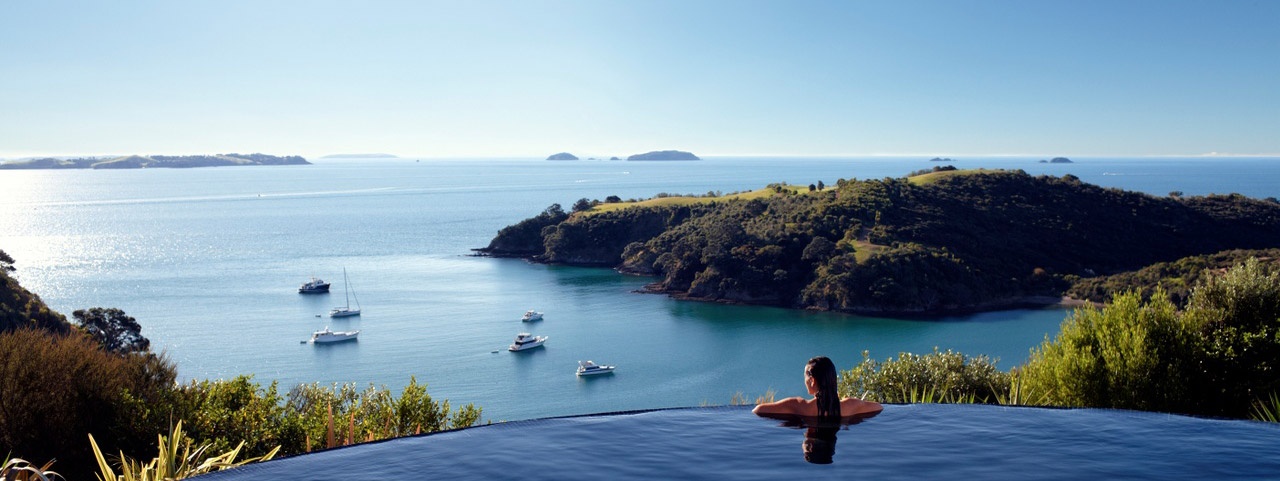 Delamore Lodge views A woman at the edge of an infinity pool looking out to ocean and island views on Waiheke Island