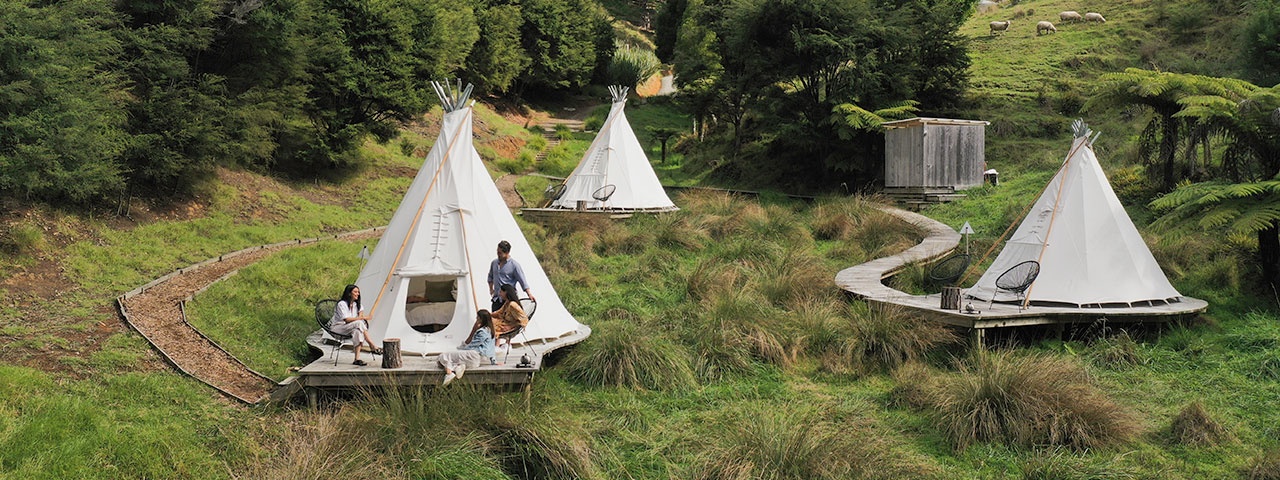 Tepee Matakana Three tepee tents with boardwalks around set on grassy hills with forest in the background